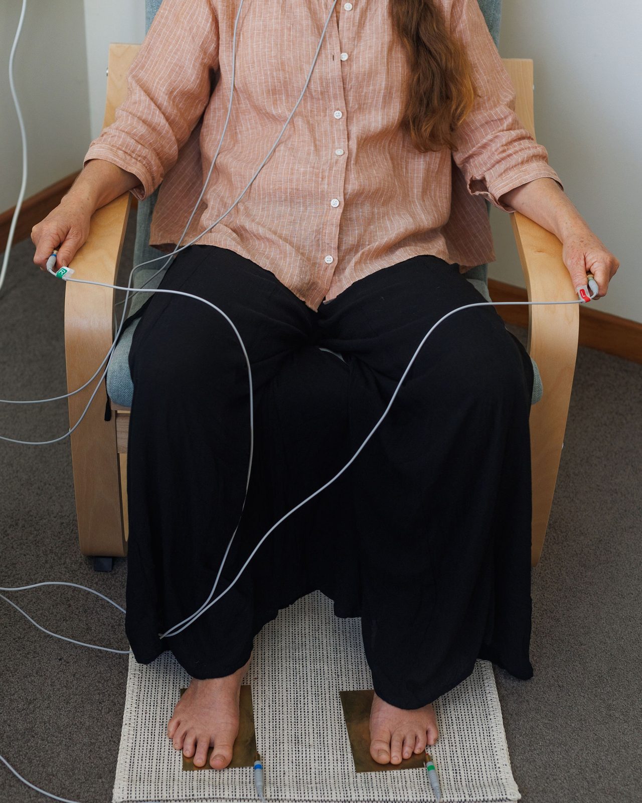 A client seated comfortably, holding the hand electrodes with her bare feet resting on brass foot plates